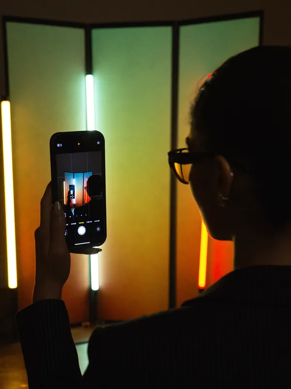 A model filming herself on a phone between tall orange and magenta light panels